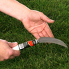 Eine Hand hält ein spezielles Rasenmesser über grünem Rasen, um diesen auf die richtige Länge zu trimmen.